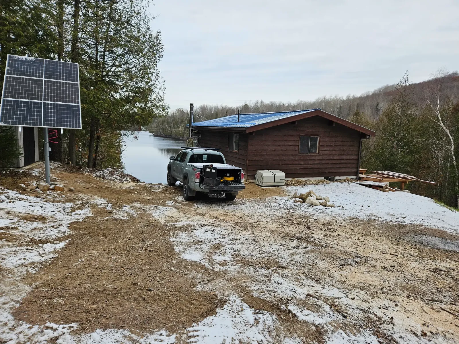 Pole-mounted solar array and standby generator beside a remote cabin in winter conditions