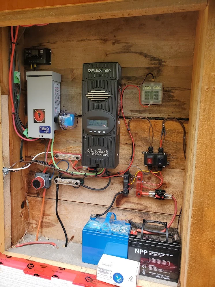 Off-grid power cabinet with inverter, charge controller, breakers, and batteries inside a wood enclosure